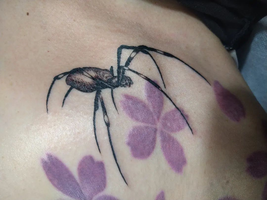 tatuaggio di un ragno con dei piccoli fiori di colore viola